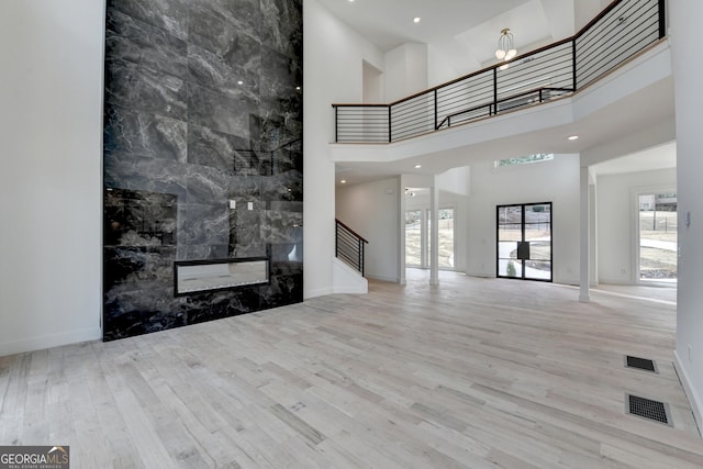 unfurnished living room featuring a towering ceiling, a high end fireplace, and light hardwood / wood-style floors