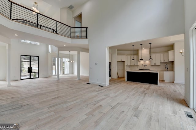 unfurnished living room with a towering ceiling, sink, an inviting chandelier, and light hardwood / wood-style floors