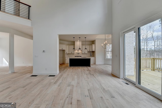 unfurnished living room featuring an inviting chandelier, light hardwood / wood-style flooring, and a high ceiling