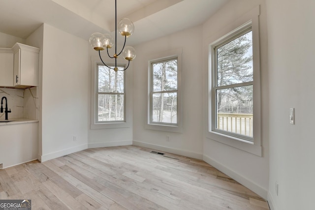 unfurnished dining area with a healthy amount of sunlight, an inviting chandelier, and light wood-type flooring