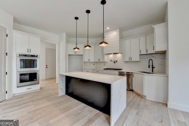 kitchen featuring premium range hood, appliances with stainless steel finishes, pendant lighting, white cabinetry, and sink