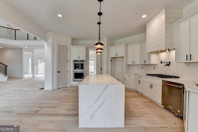 kitchen with hanging light fixtures, stainless steel appliances, light stone counters, white cabinets, and a kitchen island