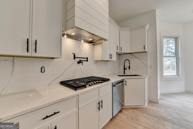 kitchen with sink, white cabinetry, stainless steel appliances, custom range hood, and light wood-type flooring