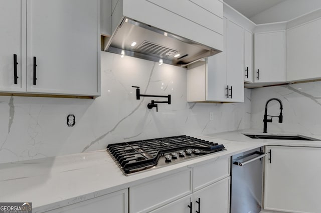 kitchen featuring range hood, sink, white cabinets, stainless steel gas cooktop, and light stone counters