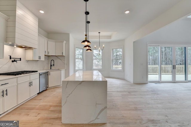 kitchen with sink, white cabinets, a kitchen island, decorative light fixtures, and a raised ceiling