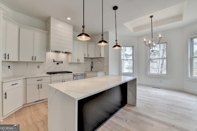 kitchen featuring gas stovetop, a raised ceiling, a kitchen island, pendant lighting, and white cabinets