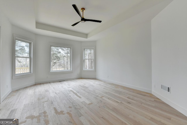 spare room featuring light hardwood / wood-style flooring, ceiling fan, and a tray ceiling