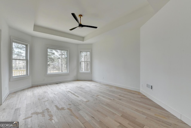 unfurnished room with a raised ceiling, ceiling fan, and light wood-type flooring