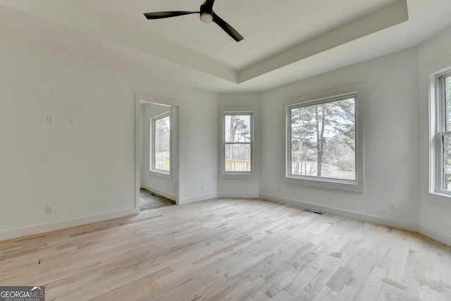 unfurnished room featuring a raised ceiling, ceiling fan, and light wood-type flooring