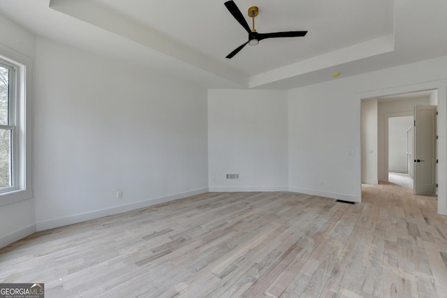 spare room featuring a tray ceiling, ceiling fan, and light wood-type flooring