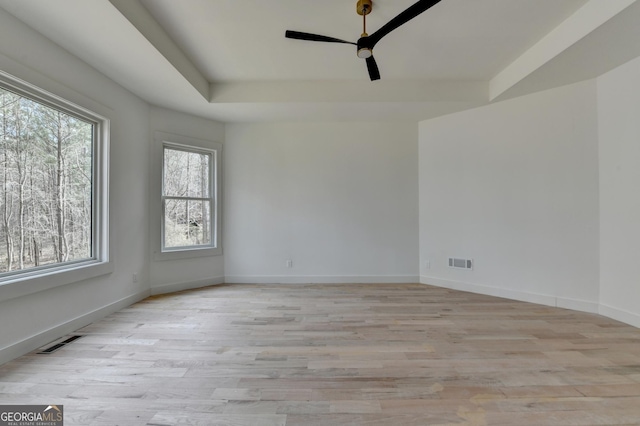 spare room with ceiling fan, a raised ceiling, and light wood-type flooring