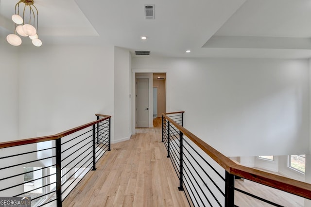 hallway with a raised ceiling, a notable chandelier, and light wood-type flooring