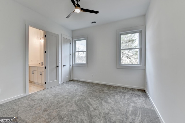 unfurnished bedroom with multiple windows, ceiling fan, light colored carpet, and ensuite bath