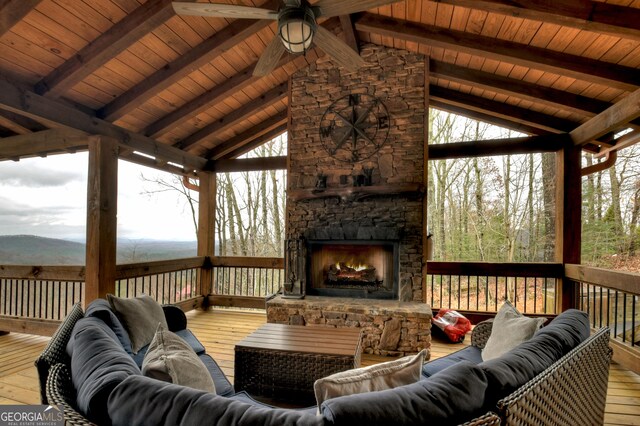 wooden deck with ceiling fan and an outdoor stone fireplace