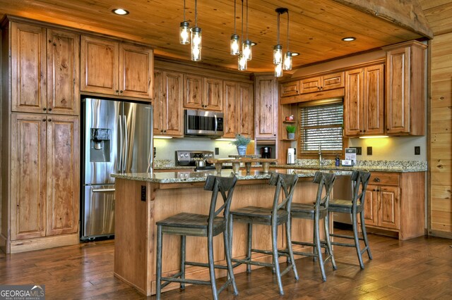 kitchen with appliances with stainless steel finishes, light stone counters, dark hardwood / wood-style floors, a kitchen island, and hanging light fixtures