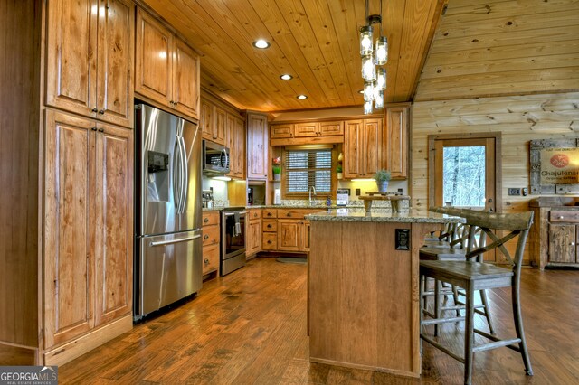 kitchen with light stone countertops, appliances with stainless steel finishes, a kitchen breakfast bar, decorative light fixtures, and dark hardwood / wood-style floors