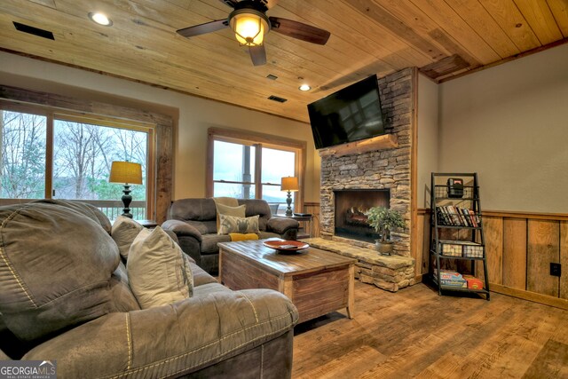 living room featuring light wood-type flooring, a stone fireplace, wooden ceiling, and wood walls