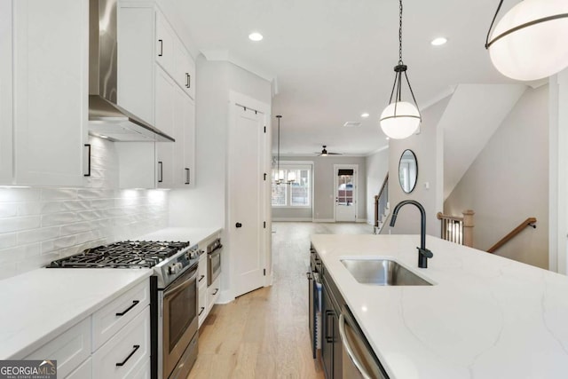 kitchen featuring light stone countertops, stainless steel appliances, sink, wall chimney range hood, and hanging light fixtures