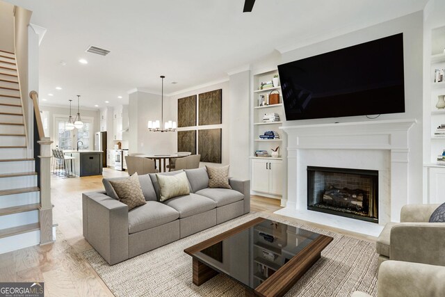 living room featuring ceiling fan with notable chandelier, light hardwood / wood-style floors, built in features, and crown molding