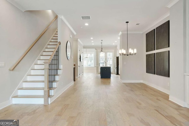 foyer entrance with sink, ornamental molding, a notable chandelier, and light wood-type flooring