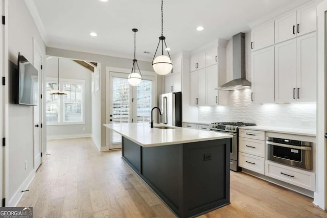 kitchen with pendant lighting, a kitchen island with sink, white cabinets, wall chimney range hood, and stainless steel appliances