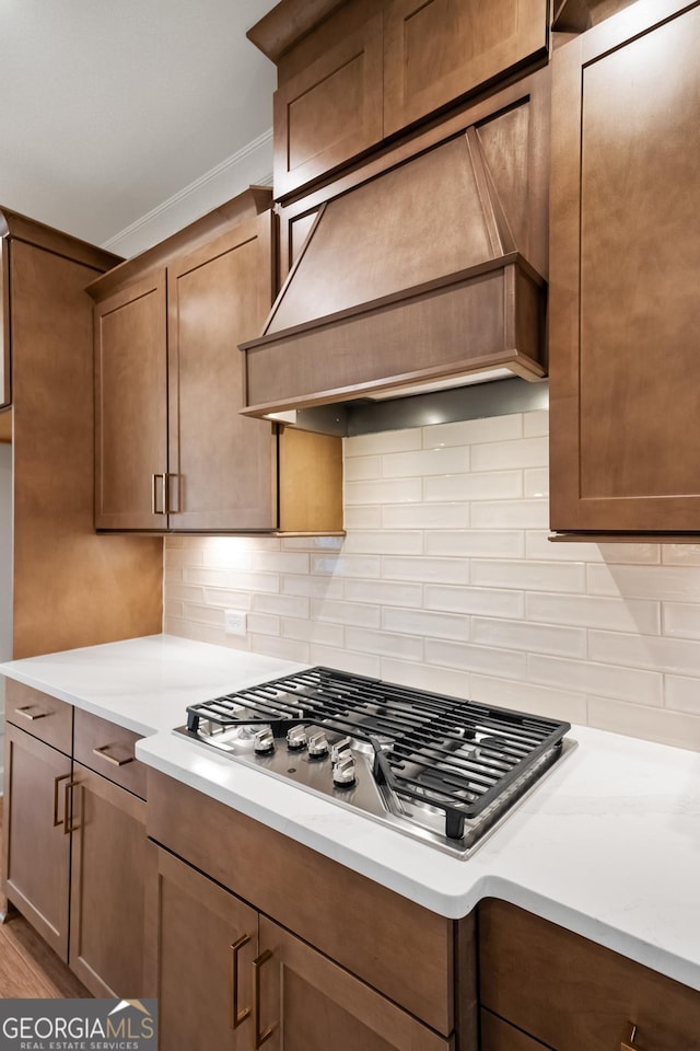 kitchen featuring tasteful backsplash, stainless steel gas cooktop, premium range hood, and ornamental molding