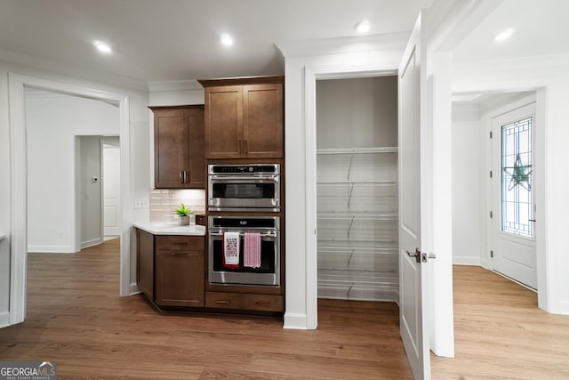 kitchen featuring double oven, light hardwood / wood-style floors, dark brown cabinets, backsplash, and crown molding