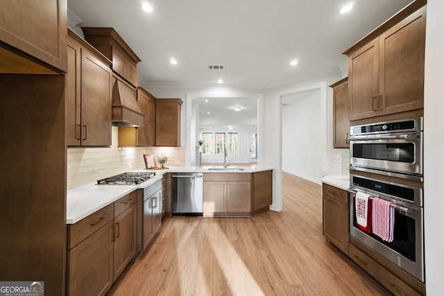 kitchen with light hardwood / wood-style floors, appliances with stainless steel finishes, decorative backsplash, custom range hood, and sink