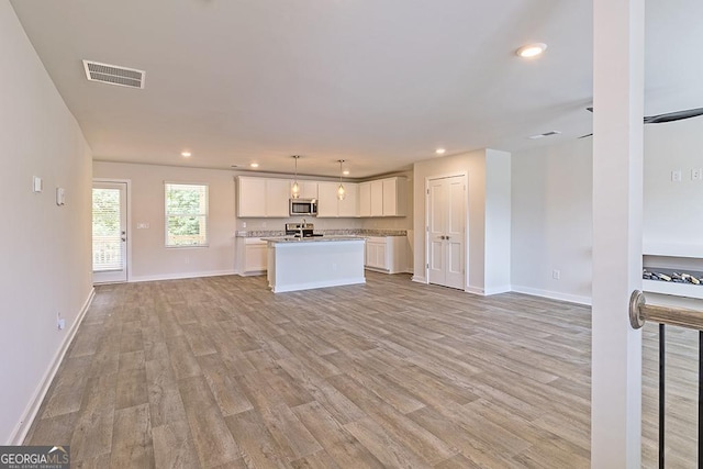 kitchen with light wood-type flooring, stainless steel appliances, decorative light fixtures, white cabinets, and an island with sink