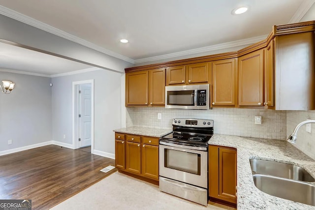 kitchen featuring sink, light wood-type flooring, ornamental molding, light stone counters, and stainless steel appliances