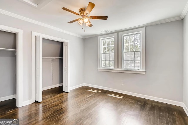 unfurnished bedroom with multiple closets, ceiling fan, dark hardwood / wood-style flooring, and ornamental molding