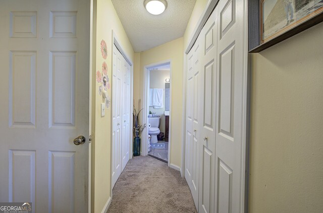 hallway featuring light colored carpet and a textured ceiling