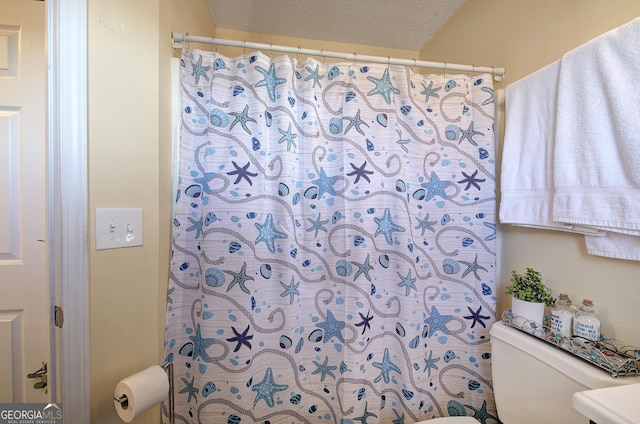 bathroom featuring a textured ceiling, toilet, and curtained shower