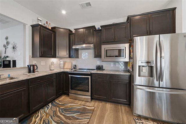 kitchen featuring appliances with stainless steel finishes, dark brown cabinetry, light hardwood / wood-style floors, and light stone counters