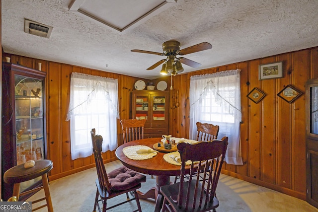 carpeted dining area with a textured ceiling, plenty of natural light, wood walls, and ceiling fan