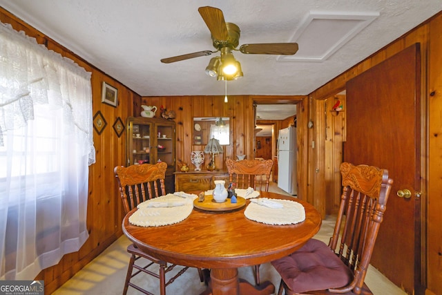 dining space with wood walls, ceiling fan, and a textured ceiling