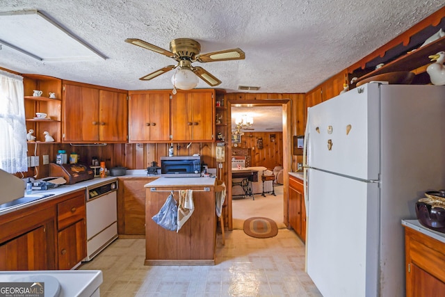 kitchen with white appliances, wooden walls, ceiling fan, a textured ceiling, and a kitchen island