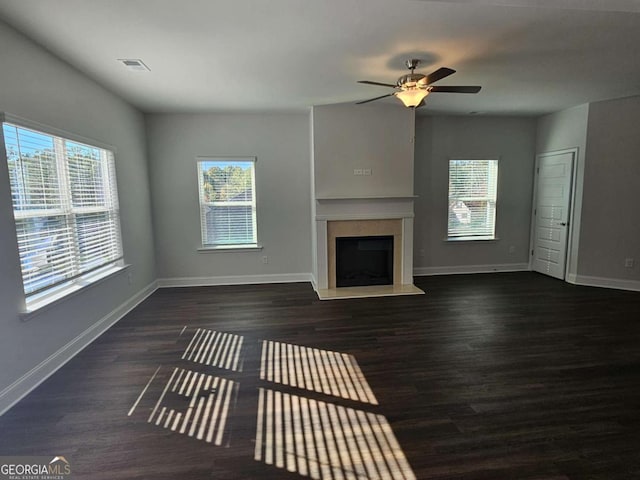 unfurnished living room with a ceiling fan, a fireplace with raised hearth, dark wood finished floors, and baseboards