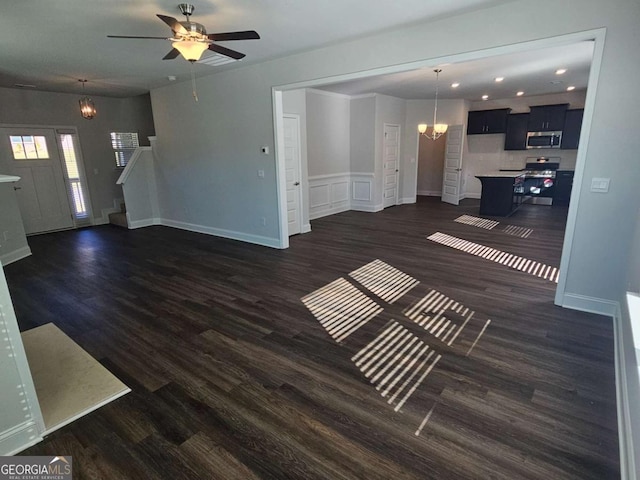 unfurnished living room with dark wood-style floors, stairway, baseboards, and ceiling fan with notable chandelier