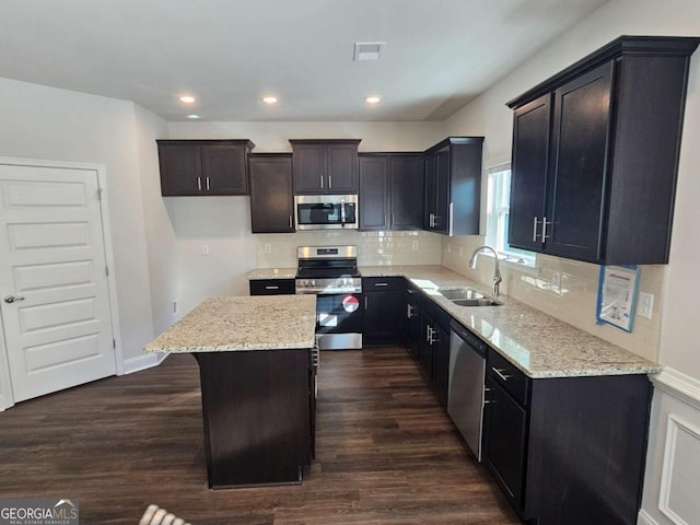 kitchen featuring dark wood-style flooring, a kitchen island, a sink, appliances with stainless steel finishes, and light stone countertops