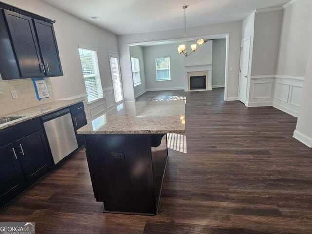 kitchen with open floor plan, stainless steel dishwasher, backsplash, light stone countertops, and dark wood-style floors