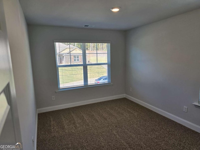 empty room with dark colored carpet, visible vents, and baseboards