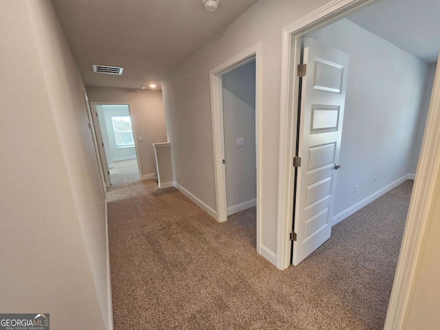 hall with an upstairs landing, carpet flooring, visible vents, and baseboards