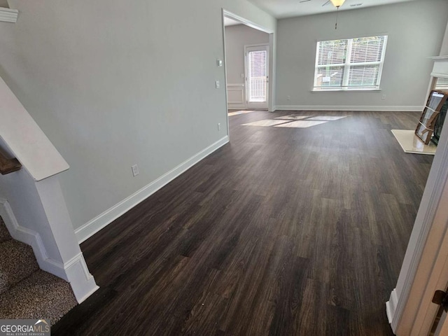 unfurnished living room with dark wood-type flooring, a fireplace with flush hearth, ceiling fan, baseboards, and stairs