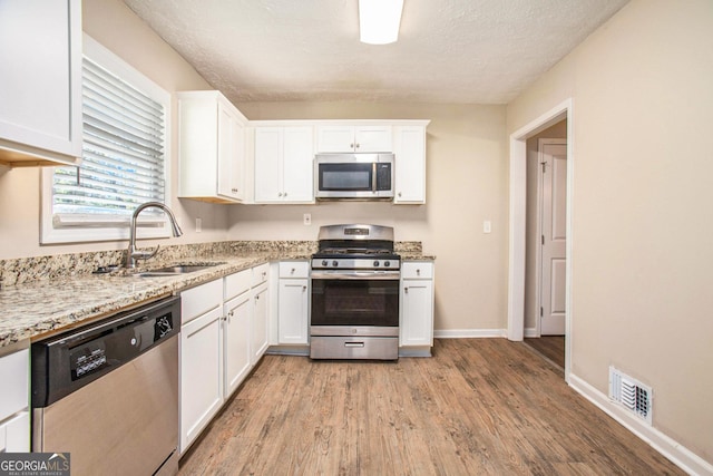 kitchen featuring white cabinetry, sink, light stone counters, light hardwood / wood-style flooring, and appliances with stainless steel finishes