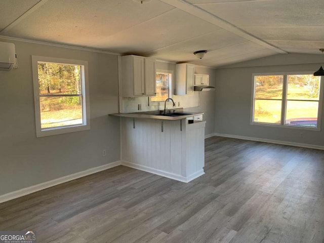 kitchen with hardwood / wood-style floors, vaulted ceiling, white cabinetry, kitchen peninsula, and a breakfast bar area