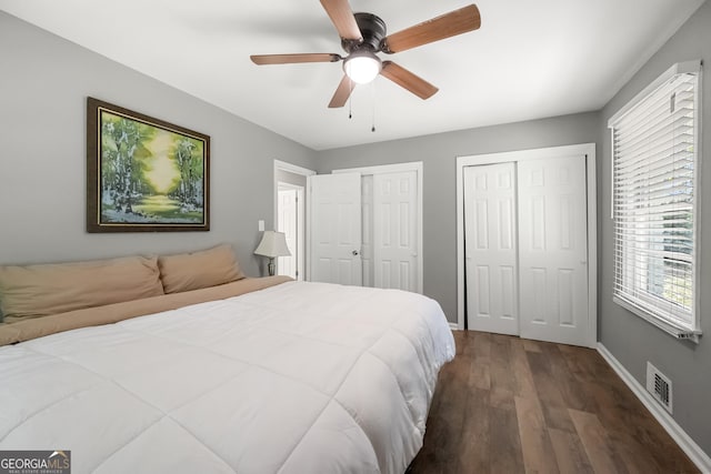 bedroom with dark hardwood / wood-style flooring, two closets, and ceiling fan