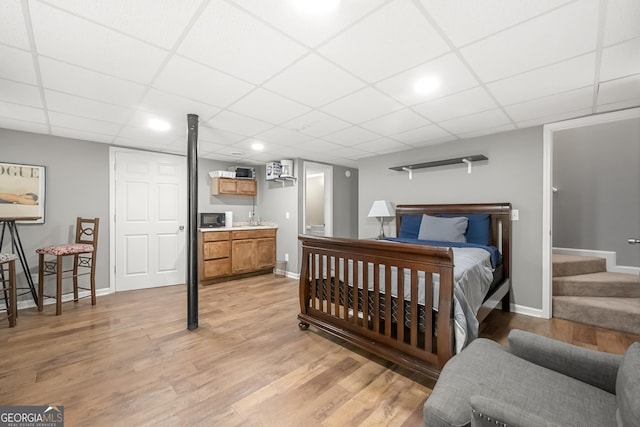 bedroom with bar area, a drop ceiling, and light hardwood / wood-style floors