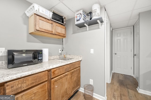 kitchen with light stone countertops, light hardwood / wood-style floors, a drop ceiling, and sink