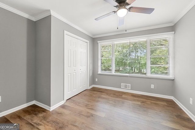 unfurnished bedroom with hardwood / wood-style floors, a closet, ceiling fan, and crown molding